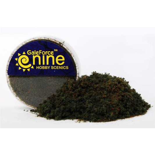 A transparent round container of Gale Force Nine Dark Conifer Flock Blend showing a textured mix of dark green and forest-toned basing material for miniatures.