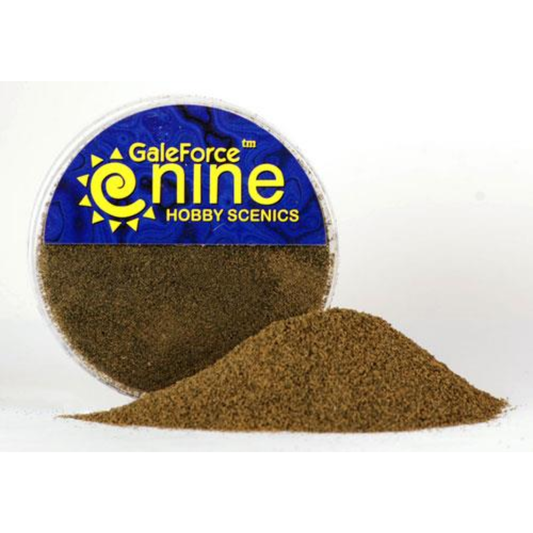 A transparent round container of Gale Force Nine Dirt Flock Foundation showing a fine-grained, deep brown earthy material for basing miniatures.
