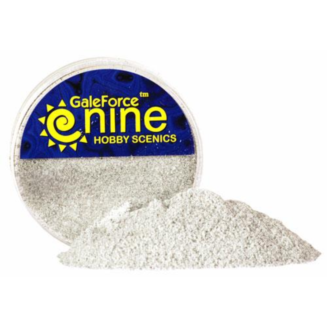 A transparent round container of Gale Force Nine Tundra/Ash Flock Foundation showing a mix of fine dark grey and charcoal basing material.