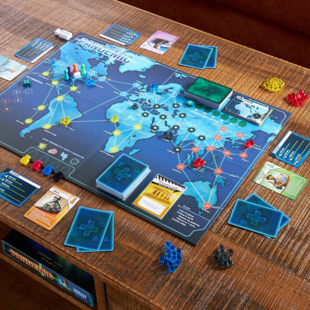 A top-down view of the Pandemic board set up with disease cubes, cards, and player pawns in various cities.